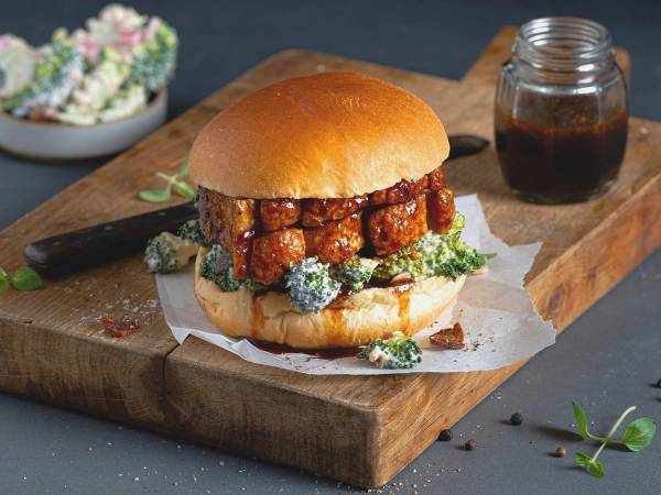 Ribbesandwich med broccolisalat på en skjærefjøl, med en liten glass med saus eller dressing ved siden av.