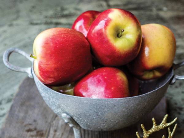 Fem røde og gule epler i en grå kurv på et bord