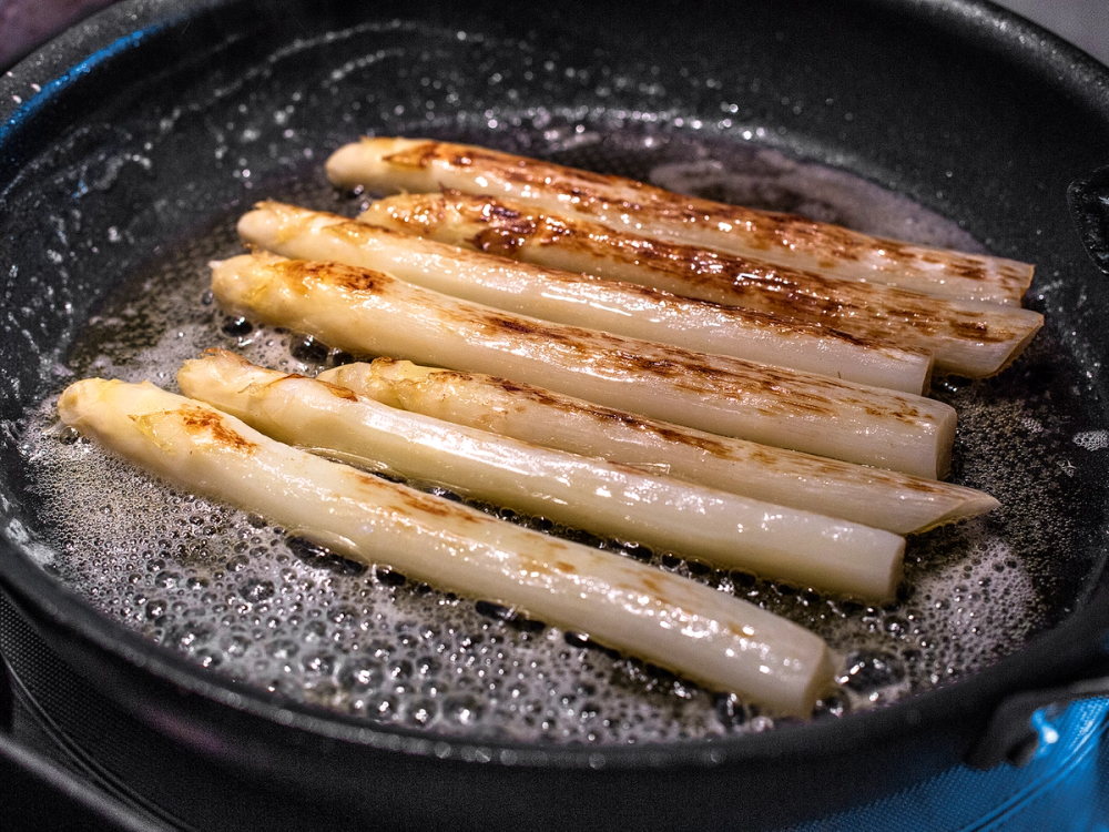 Asparges som stekes i en panne med litt fett, med gyllenbrune flekker på overflaten.