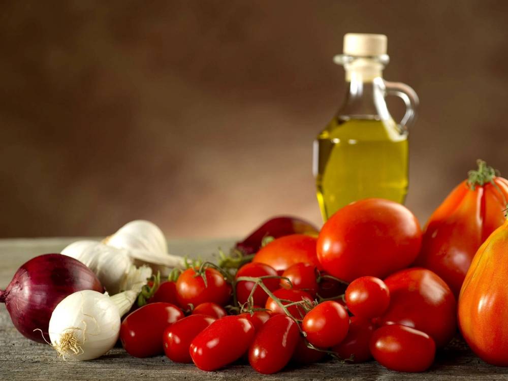 Ferske tomater, hvitløk og en flaske med olivenolje på et bord.