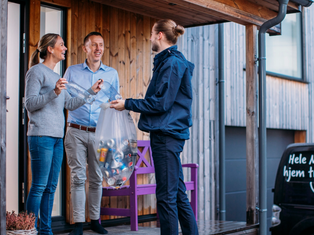 En person gir en pose med varer til to personer utenfor en bygning, mens de snakker sammen.