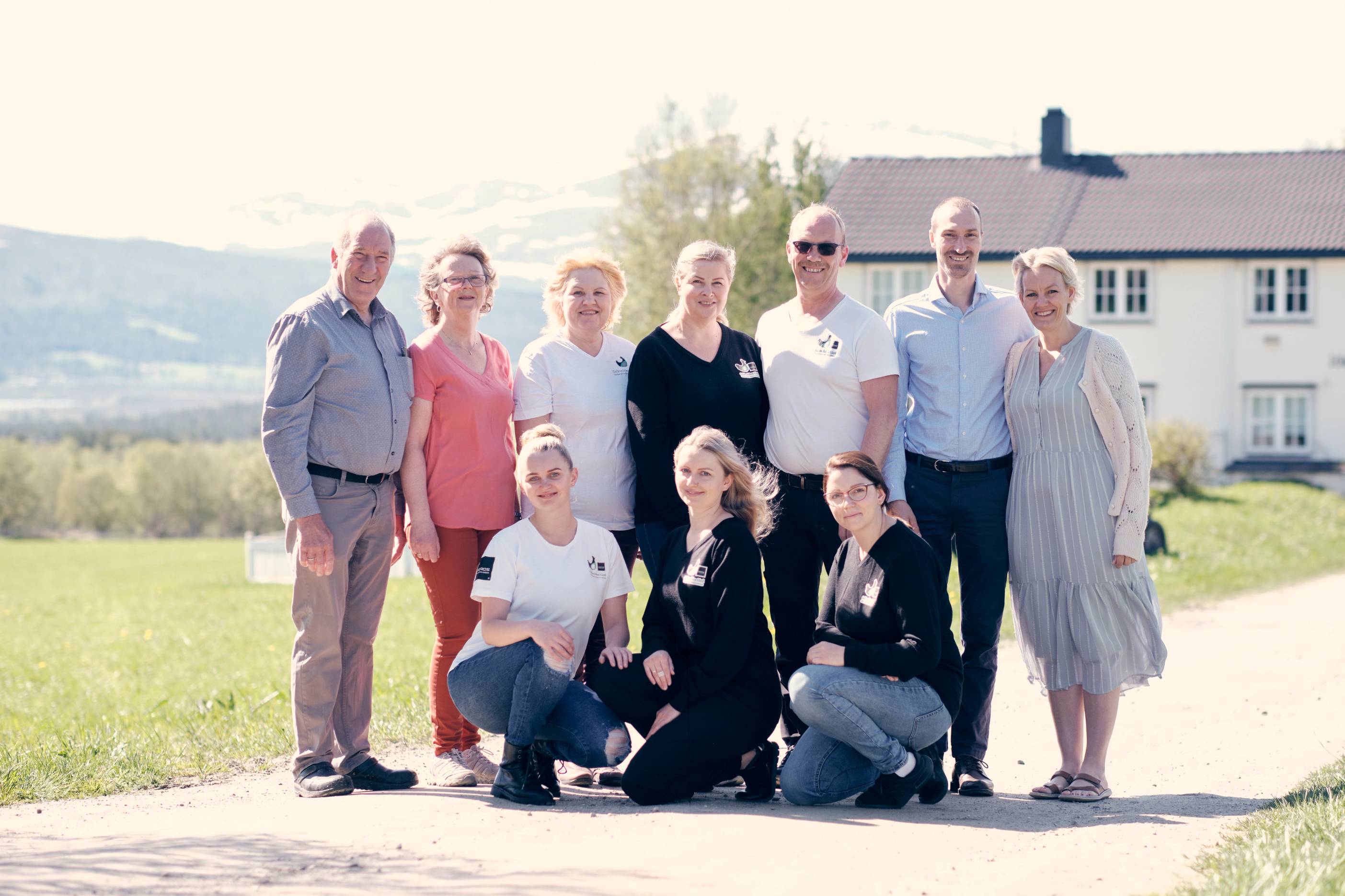 En gruppe ansatte og eldre personer samlet utendørs foran en hvit bygning, som illustrasjon av generasjoner og arbeidsmiljø.