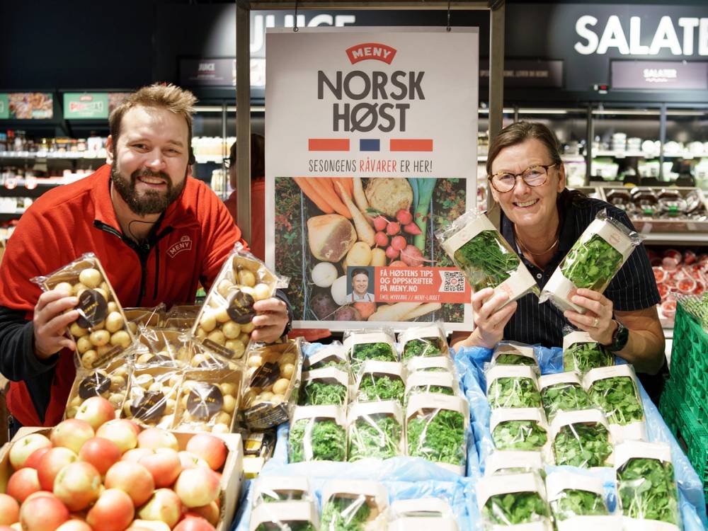 To personer handler frukt og grønnsaker i en dagligvarebutikk med en plakat for Norsk Høst i bakgrunnen.