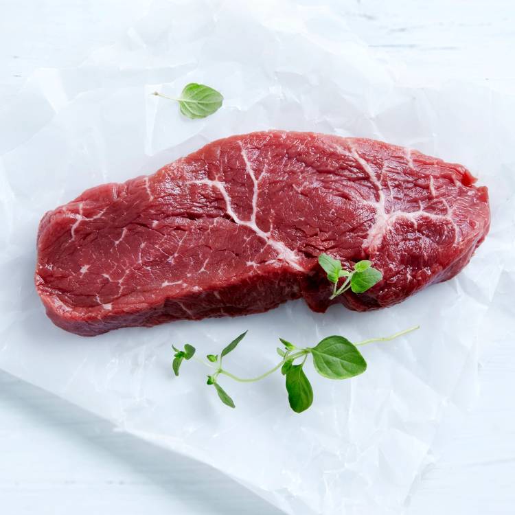 En rå ytrefilet av storfe ligger på hvitt papir med noen små grønne urter rundt.