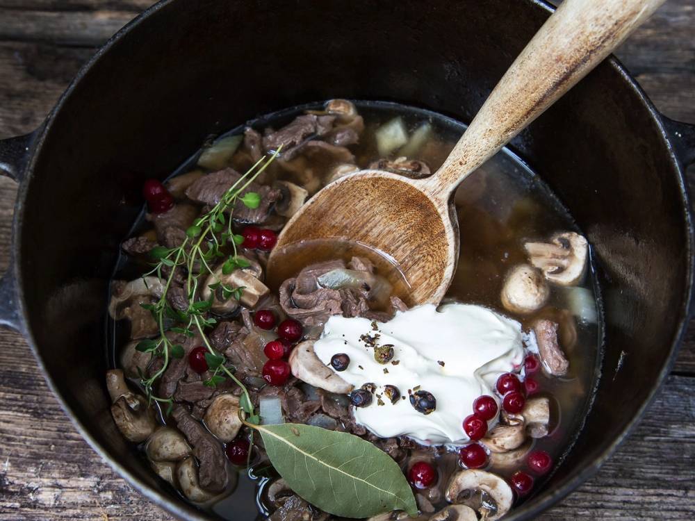 Viltgryte med sopp, krydderurter og en klatt med krem eller yoghurt i en svart gryte, med en tresleiv i.