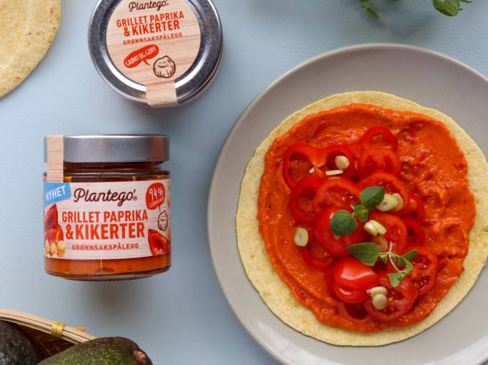 En tortilla med grillet paprika og cherrytomater, pyntet med basilikumblad, på en tallerken.