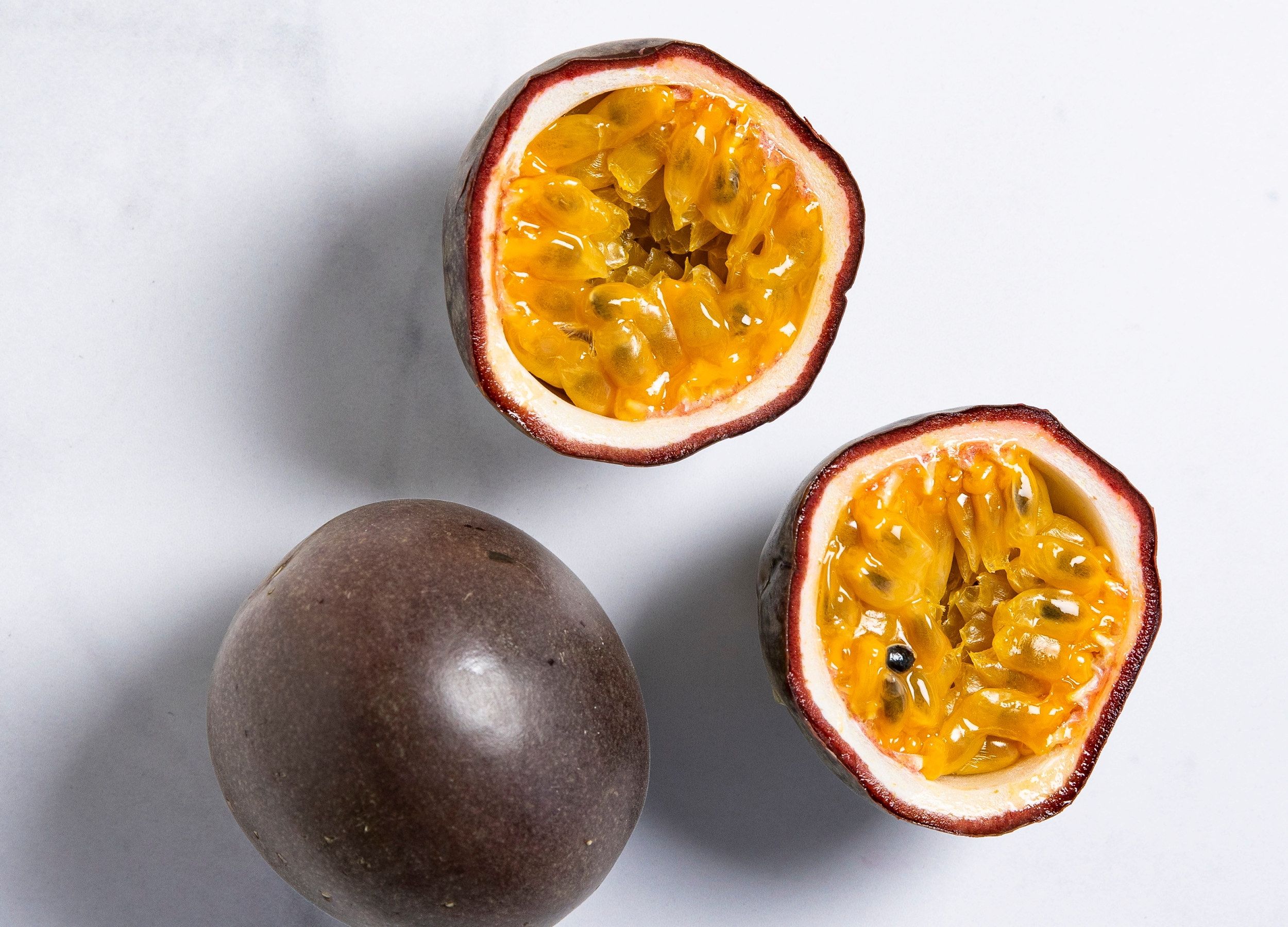 To pasjonsfrukter, en hel og en delt, med gul fruktkjøtt og svarte frø, på en lys bakgrunn.
