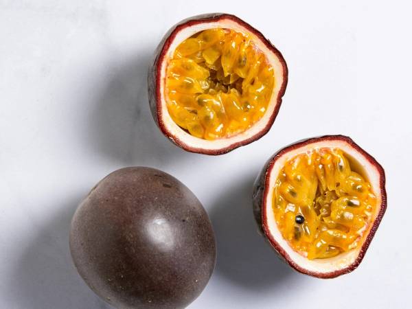 To pasjonsfrukter, en hel og en delt, med gul fruktkjøtt og svarte frø, på en lys bakgrunn.