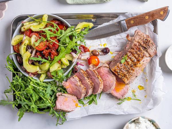 Svinefilet med tatziki, servert med en salat av grønnsaker og urter på et hvitt fat.