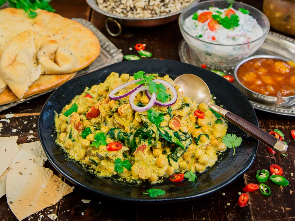 En tallerken med indisk inspirert rett med bønner og linser, pyntet med løk og chili, omgitt av naanbrød og små boller med saus.