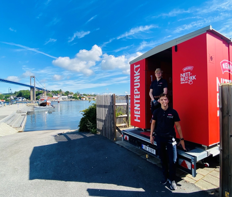 Hentepunkt med to ansatte ved en rød container ved vannet, med en bro og bygninger i bakgrunnen.