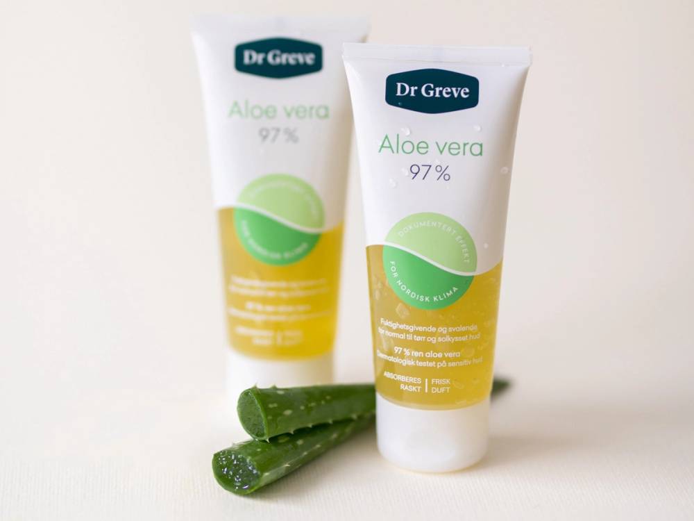 To tuber av Dr Greve Aloe Vera med en bit aloe vera-plante ved siden av, på en hvit bakgrunn.