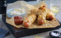 Innbakte pølser med revet ost på en serveringsplate med tilbehør som ketchup og potetsalat.