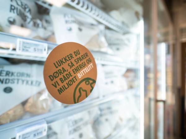 En butikkhylle med ulike poser og en rund, oransje etikett som oppfordrer til å spare miljøet ved å redusere plastbruk.