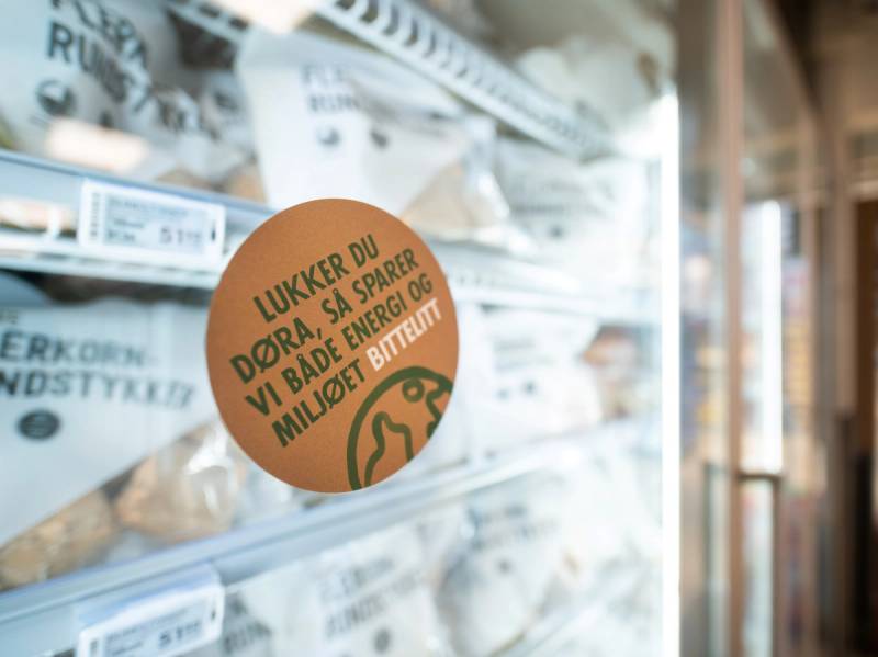 En butikkhylle med ulike poser og en rund, oransje etikett som oppfordrer til å spare miljøet ved å redusere plastbruk.