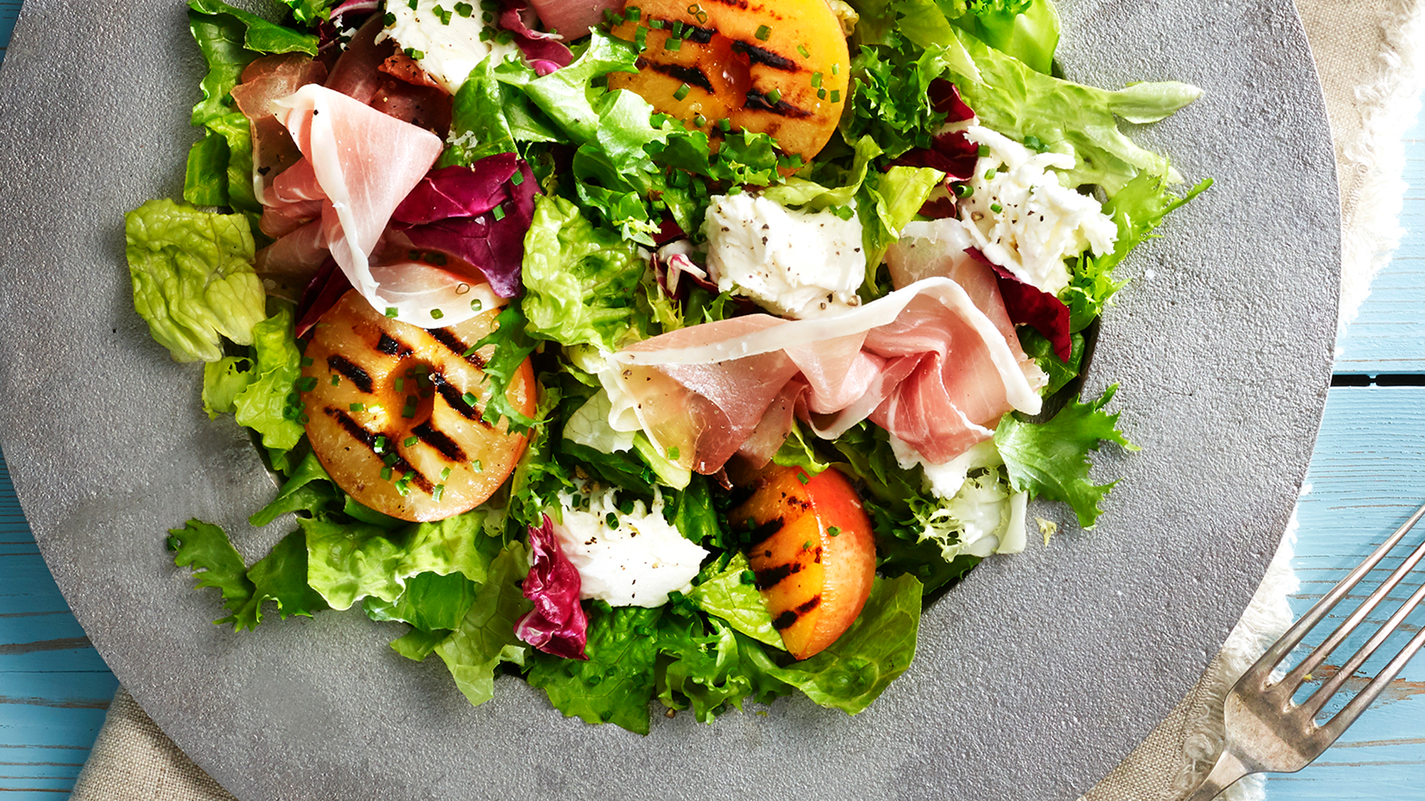 Salat med skinke, cherrytomater, salatblader og ost på en grå tallerken.