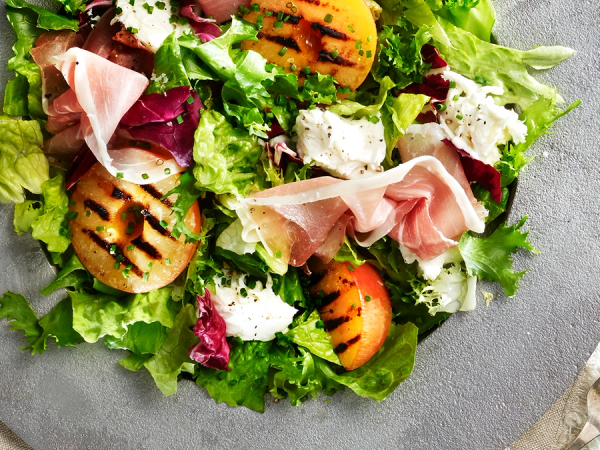 Salat med skinke, cherrytomater, salatblader og ost på en grå tallerken.