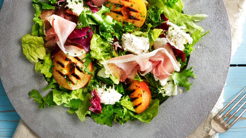 Salat med skinke, cherrytomater, salatblader og ost på en grå tallerken.