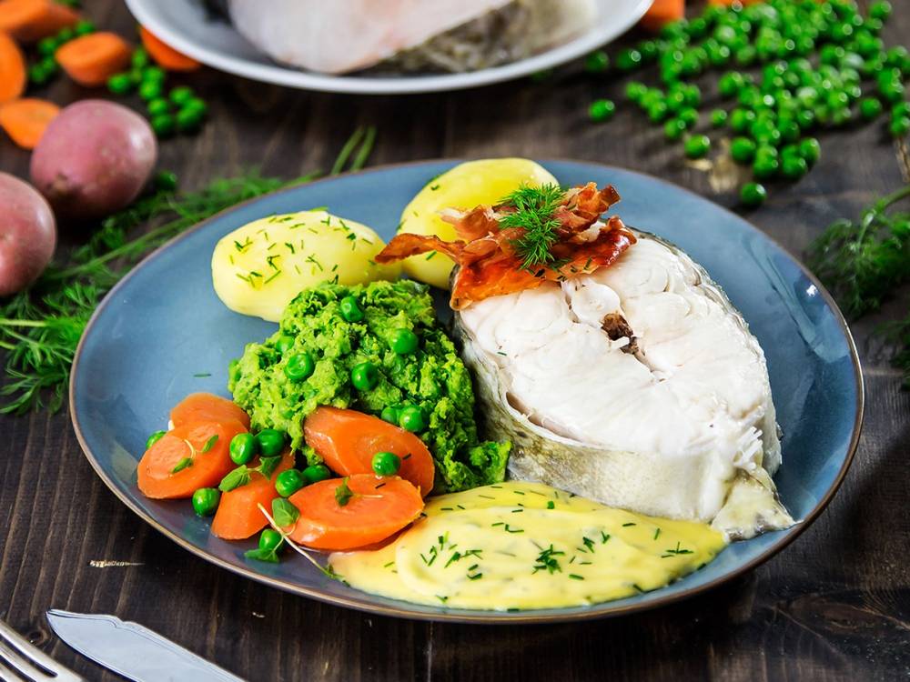 Skrei-hode servert med potetmos, gulrot og brokkoli på en blå tallerken.