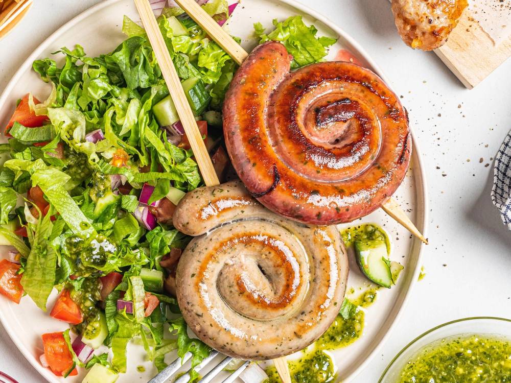 To spiddede pølser, en med spiralformet saus, ligger på en tallerken sammen med en frisk salat og noen grønnsaker.