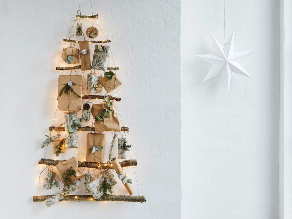 En julekalender laget av tre med små pakker og dekorasjoner hengt opp på en vegg, med en stor hvit julestjerne til høyre.