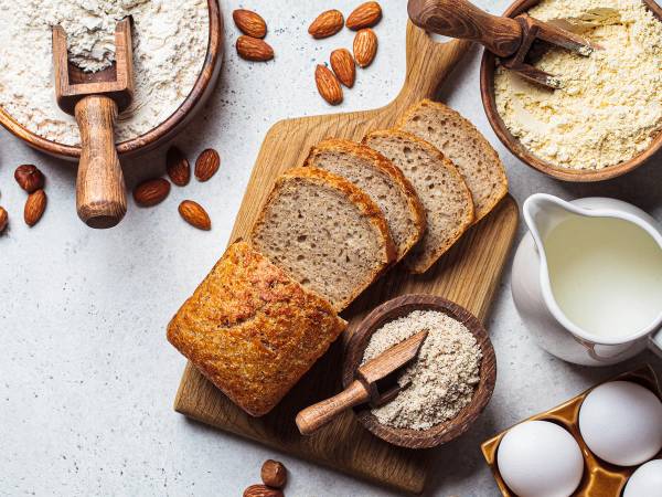 Glutenfritt brød og mel på et kjøkkenbord med nøtter og egg rundt.