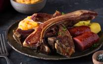 Pinnekjøtt med kokte poteter og gulrot på en svart tallerken, servert med litt grønt som pynt.