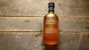 En liten flaske med Odelia-logo står på et trebord av treverk.