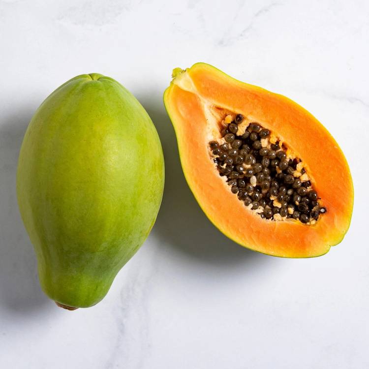 En hel grønn papaya og en halvert papaya med oransje kjøtt og svarte frø på en hvit bakgrunn