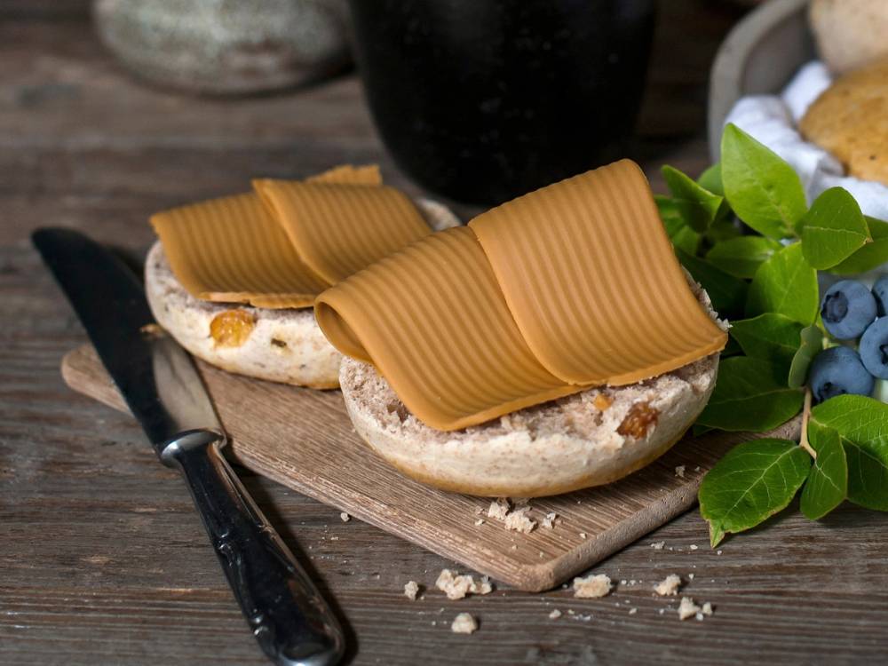 To scones med karamellfarge og en klatt smør på en treplate, omgitt av blåbær og grønn blader, med en kniv ved siden av.