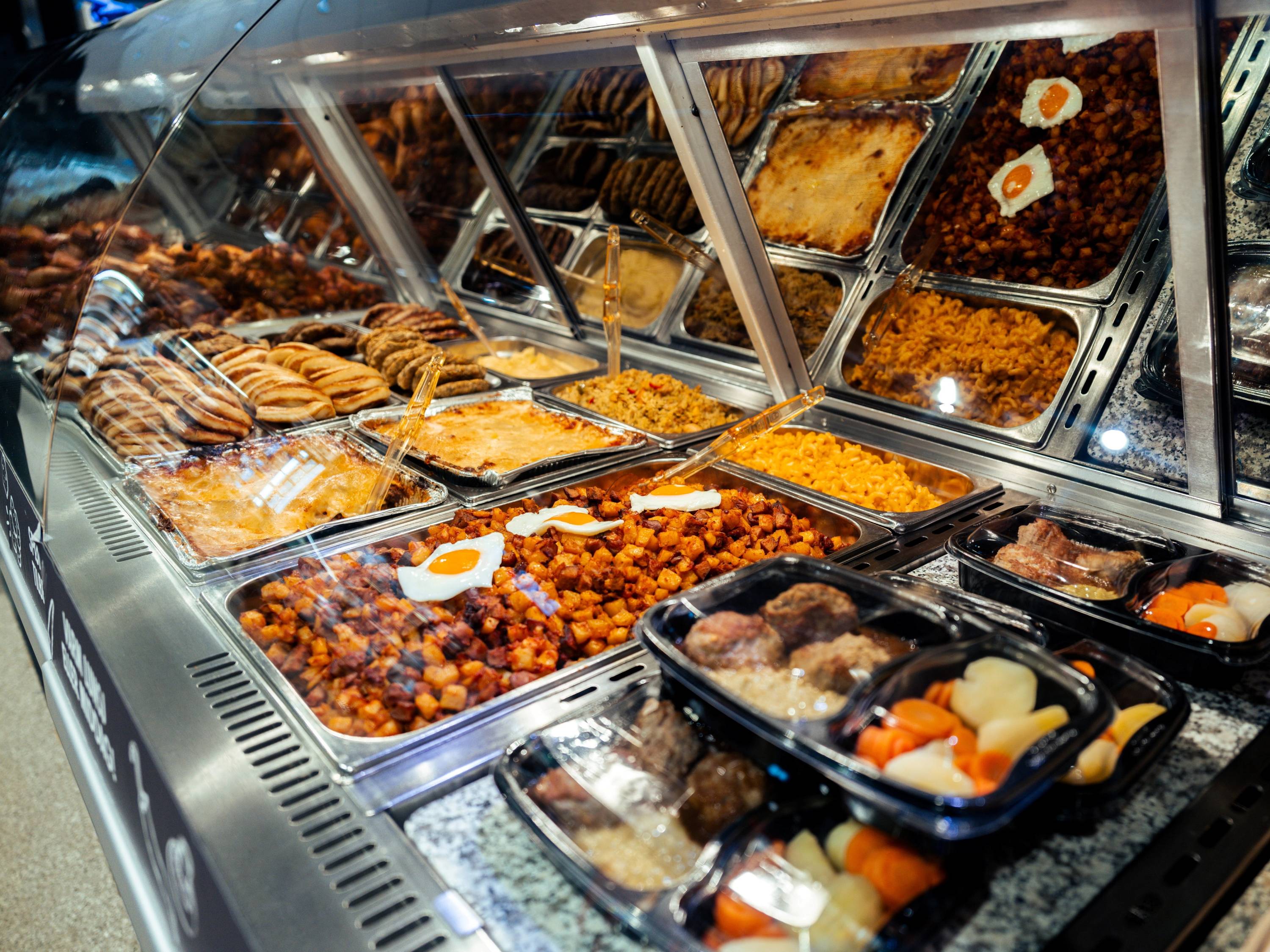 Ulike varme retter og bakverk i en matbutikkdisk på Tveita, med en glasskuff som viser maten.