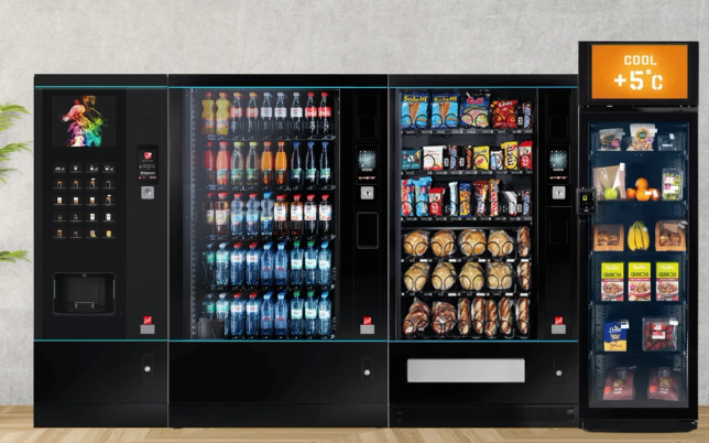 Automat for snacks og drikkevarer med ulike utvalg av brus, kjeks og snacks, samt en liten skjerm som viser temperaturen +5°C.