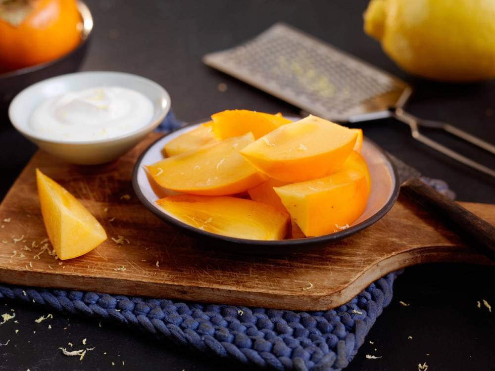 Oppskåret persimon på en tallerken med en skje og en skål med yoghurt ved siden av.
