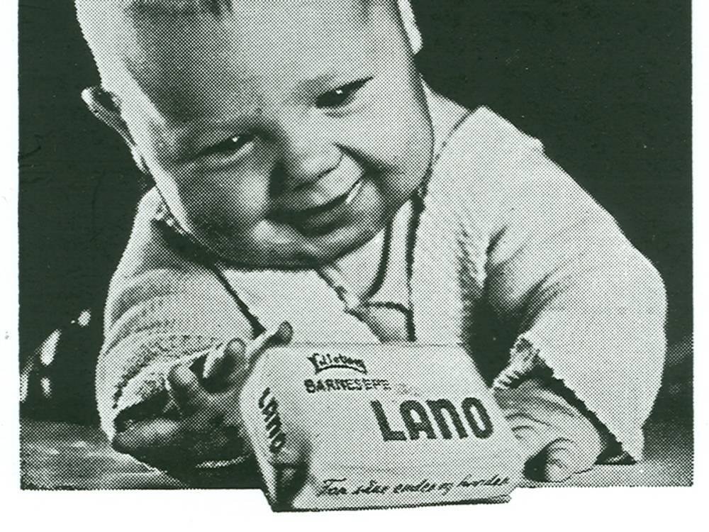 En person i 1950-talls klær holder en eske med Lano-barberingskrem, med en uklar bakgrunn.