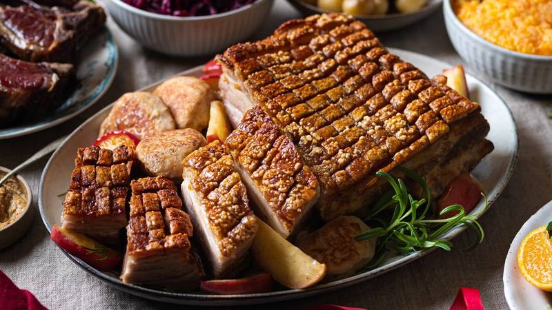 Julebord med ribbe, medisterkaker, surkål, poteter og tilbehør på et dekket bord.