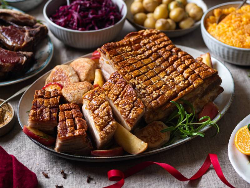 Julebord med ribbe, medisterkaker, surkål, poteter og tilbehør på et dekket bord.