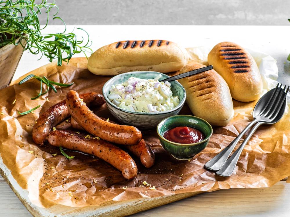 Kyllingpølse med løksalat og brød på et serveringsfat med ketchup og bestikk.