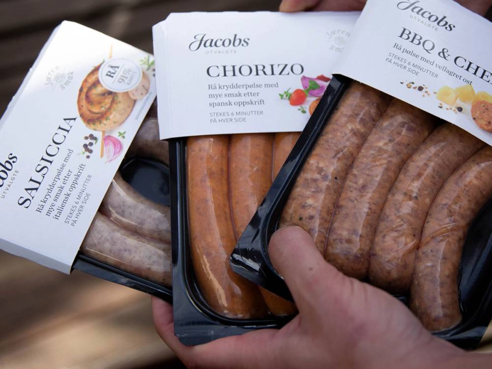 Person som holder i en pakke med Jacobs pølser, klar til grilling eller servering.