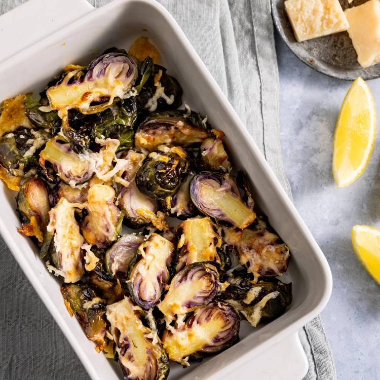 Parmesangratinerte rosa kål i en hvit ildfast form, med sitronbåter ved siden av.