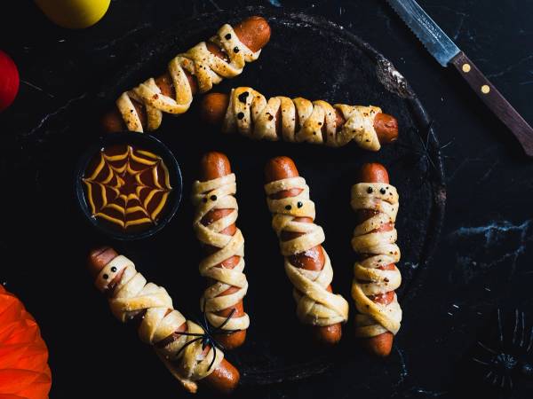 Pølsepynt med spindelvev og små spøkelser laget av mat, satt på et svart fat til Halloween-feiring.