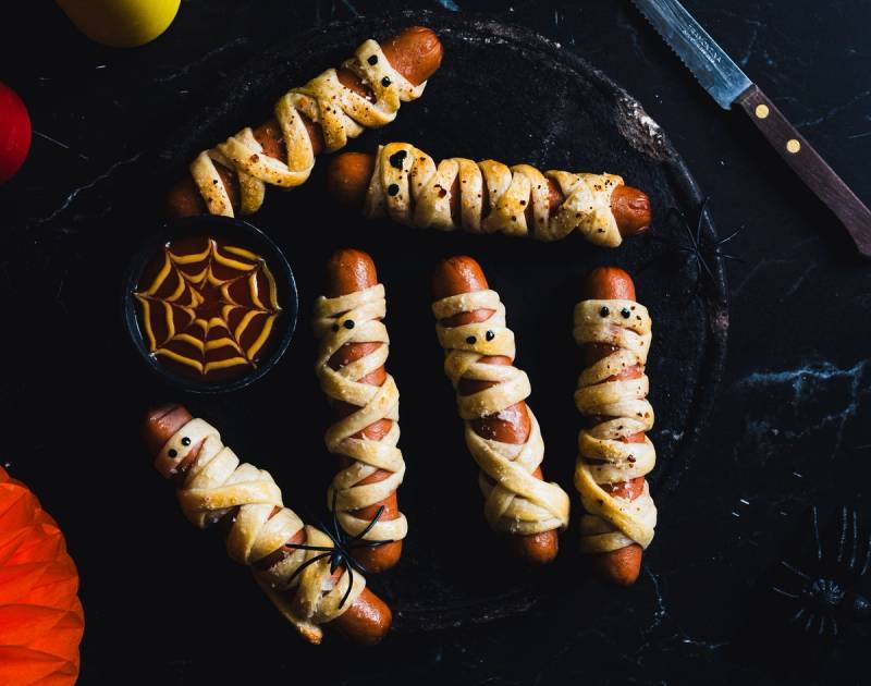 Pølsepynt med spindelvev og små spøkelser laget av mat, satt på et svart fat til Halloween-feiring.