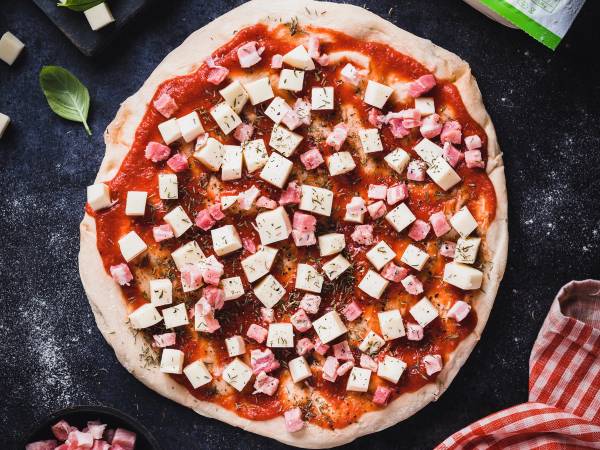 En ferdig pizza med tomatsaus, ost, skinke og tofu på en svart stekeplate