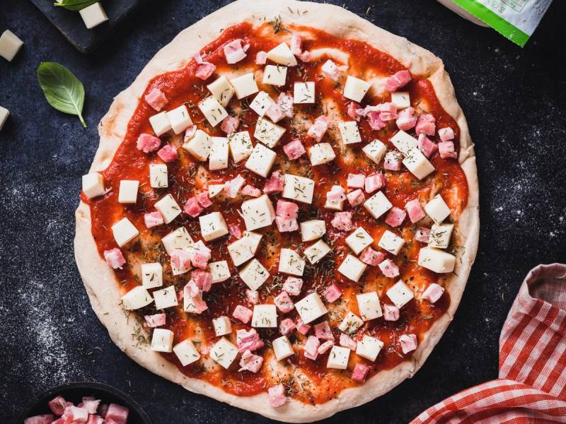 En ferdig pizza med tomatsaus, ost, skinke og tofu på en svart stekeplate