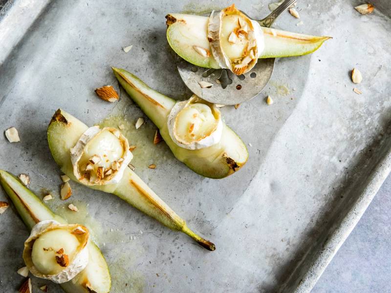 Ferske pærehalser fylt med geitost og toppet med hakkede nøtter, servert på et stekebrett.