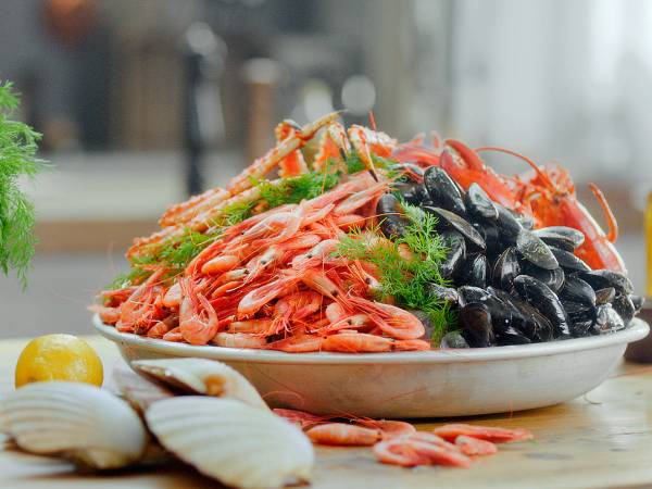 Et stort fat med skalldyr, inkludert reker, blåskjell og krabber, pyntet med grønn dill, på et kjøkkenbord.