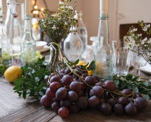 Nyttårsbord med vinflasker, blomster og en klynge med røde og blå druer på et treverk, klar for feiring.