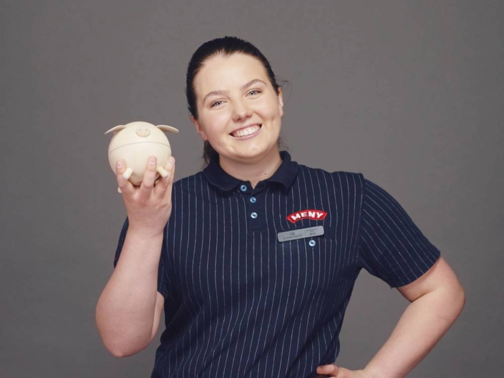 Person holder en hvit sparegris i hånden, iført en blå stripete skjorte med en logo på brystet.