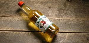 En flaske med eplejuice ligger på et trebord, med etiketten synlig.