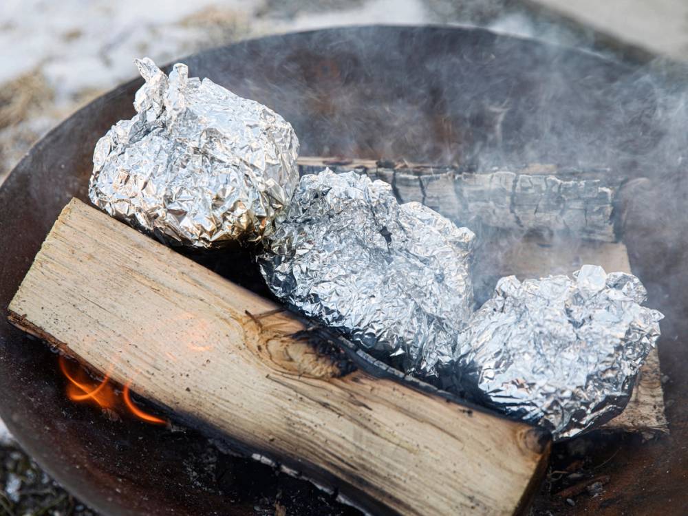 Bakte poteter innpakket i aluminiumsfolie på et bål, med glødende vedkubber under.