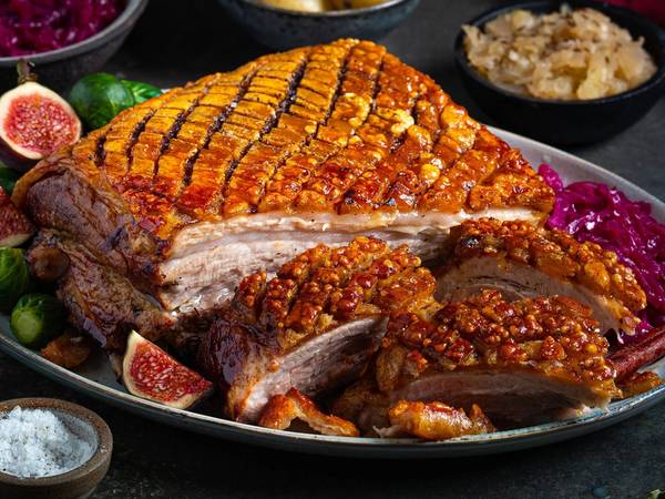 Ribbe med sprø svor, servert med rosenkål, poteter, surkål og julekrydder på et fat.
